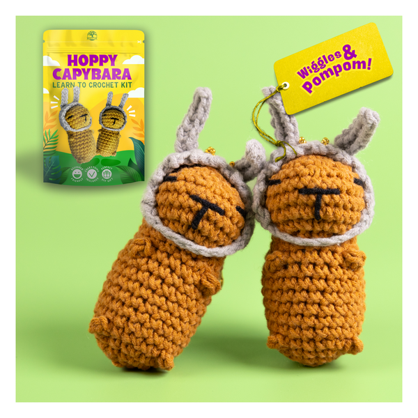 Crocheted capybara toys with packaging and tag on a green background