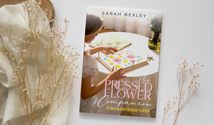 Physical book cover of 'The Pressed Flower Companion: A Journey from Hobbyist to Artist' by Sarah Bexley, styled flat-lay with dried baby's breath sprigs and sheer cream fabric on a white surface.