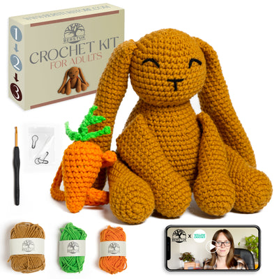 Crocheted bunny and carrot set with yarn, hook, and packaging on a white background