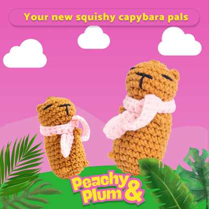 Two knitted capybara toys with scarves on a pink background with 'Peachy Plum' branding.