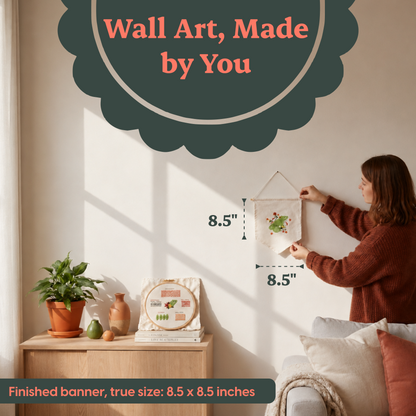 A woman hangs a small woven wall art piece on a cream wall in a styled living room. The banner has a frog design and includes overlaid size measurements of 8.5 inches.