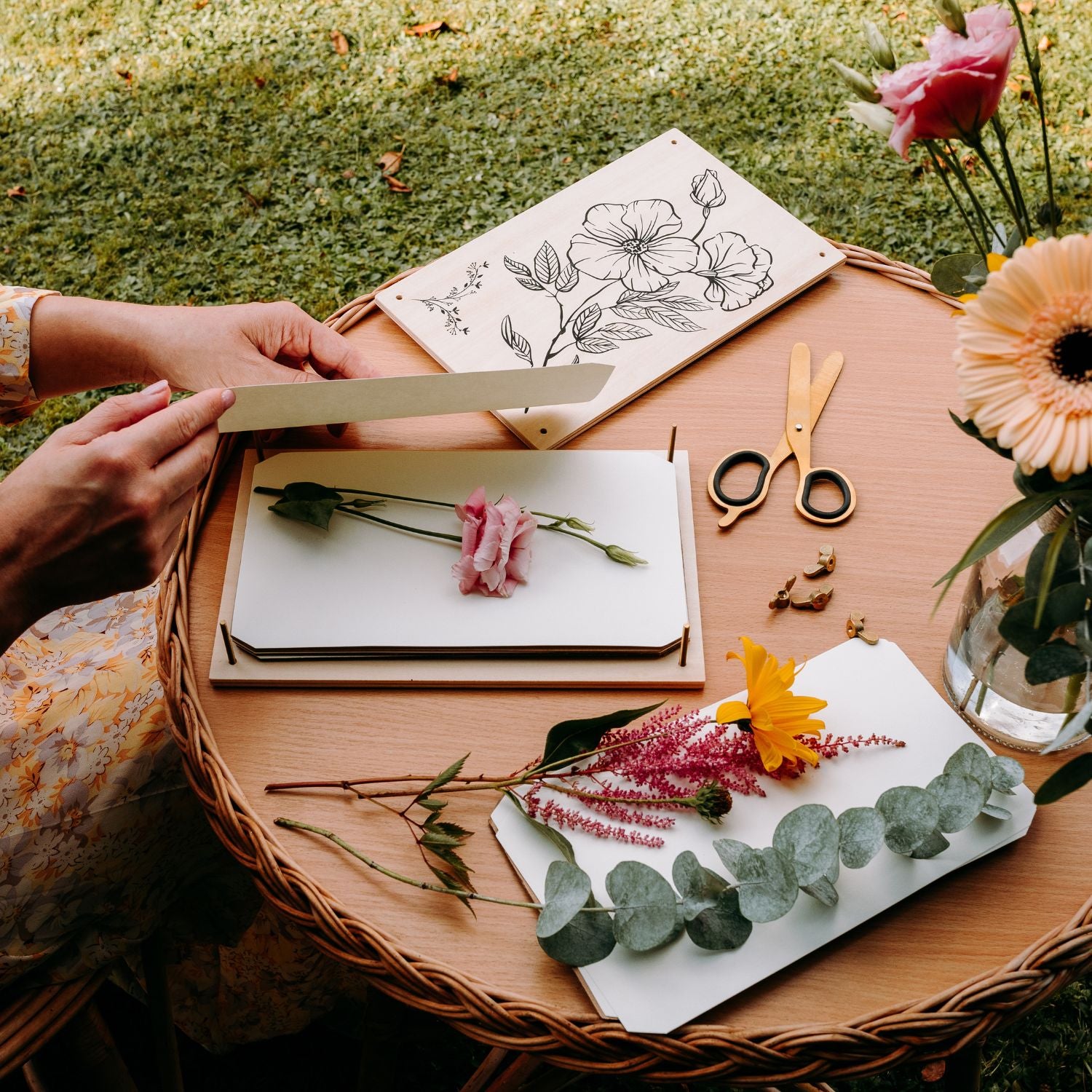 a flower press with flowers inside it on a table in a garden with blotting paper held by a flower preservation artist