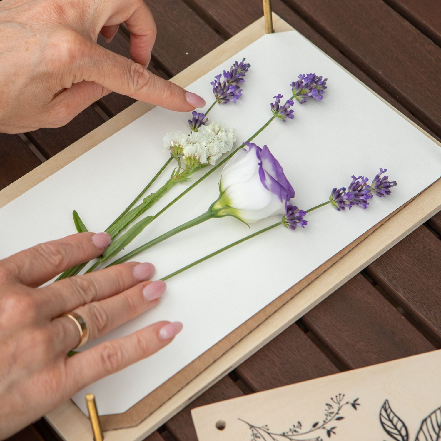 a flower preservation artist gently positioning flowers on blotting paper on a wooden table