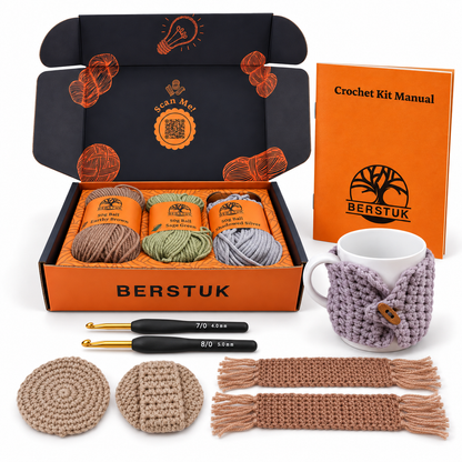 A Berstuk crochet kit set displayed on a white background, including an open navy blue and orange box with three yarn balls, a crochet kit manual, a crocheted mug cozy over a white mug, two crochet hooks, two circular face scrubbies, and two fringed bookmarks in assorted neutral and earthy tones.