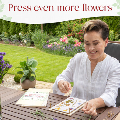 Woman arranging pressed flowers on a flower press at an outdoor garden table