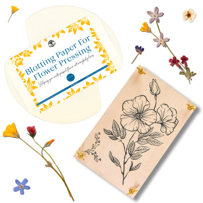 Wooden flower press with floral print and blotting paper package, surrounded by pressed flowers